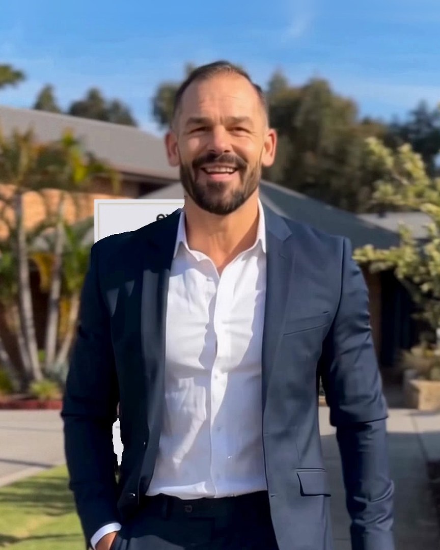 Matt Manser in a navy suit, on the phone outside one of his listings